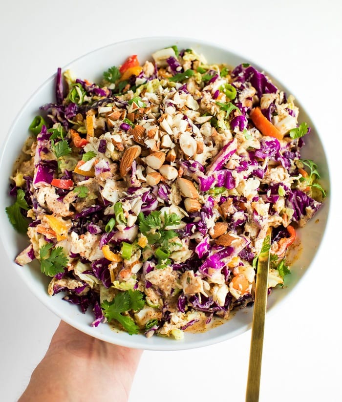 Crunchy asian salad in a white bowl with gold spoon being held by a woman's hand. 