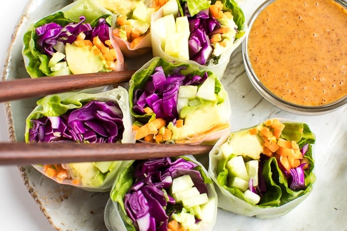 PIN THIS --> EASY Vegetable Spring Rolls with a Delicious Peanut Sauce Fresh vegetables spring rolls with homemade peanut sauce being picked up with wooden chopsticks.