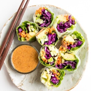 Fresh vegetables spring rolls on a rustic plate with homemade peanut sauce. Chopsticks are laying on the plate as well.