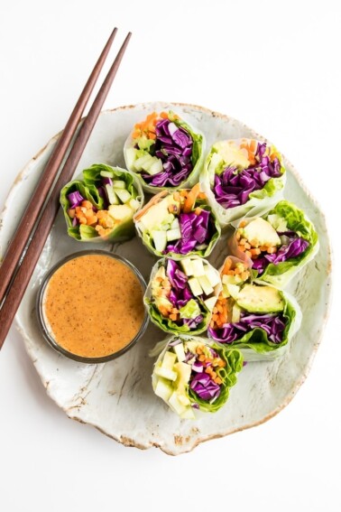 Fresh vegetables spring rolls on a rustic plate with homemade peanut sauce. Chopsticks are laying on the plate as well.