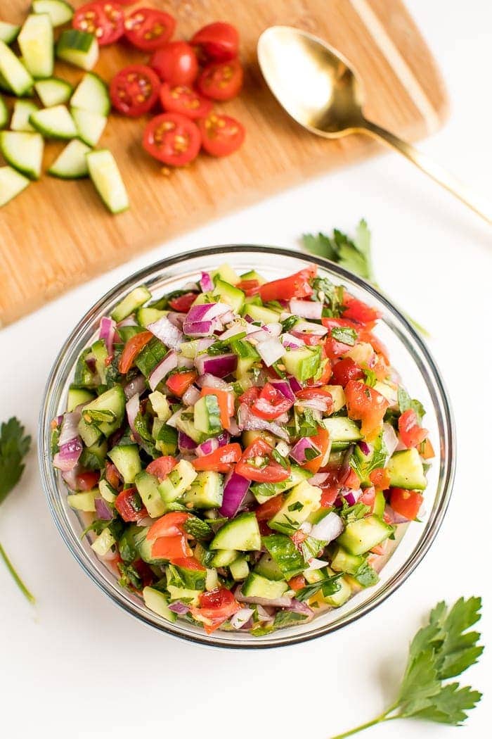 Clear glass bowl filled with Israeli salad, a blend of tomatoes, cucumbers and red onion. 