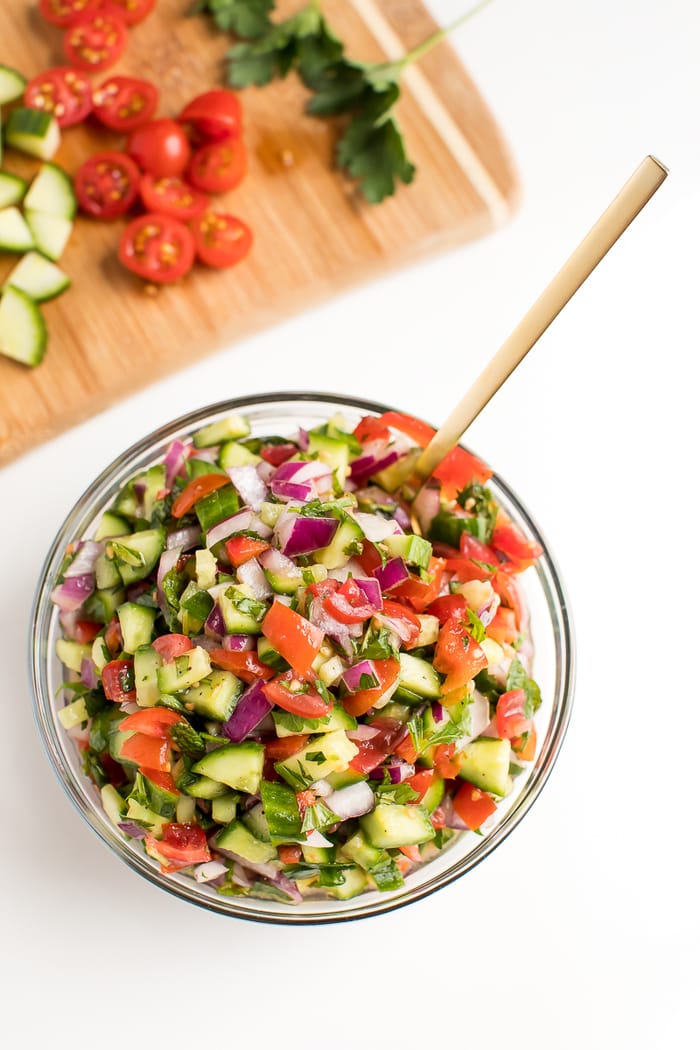 Clear glass bowl filled with Israeli salad, a blend of tomatoes, cucumbers and red onion. 