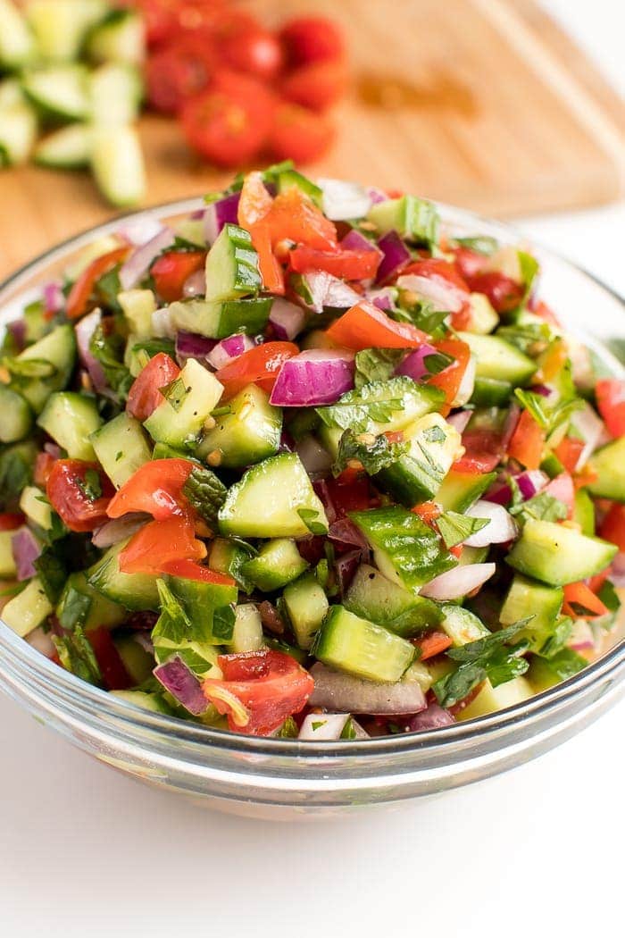 Clear glass bowl filled with Israeli salad, a blend of tomatoes, cucumbers and red onion. 