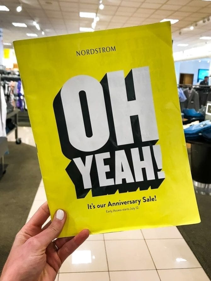 Woman's hand holding a yellow flyer from Nordstrom's Anniversary sale. The flyer says "Oh yeah! It's our Anniversary Sale!"