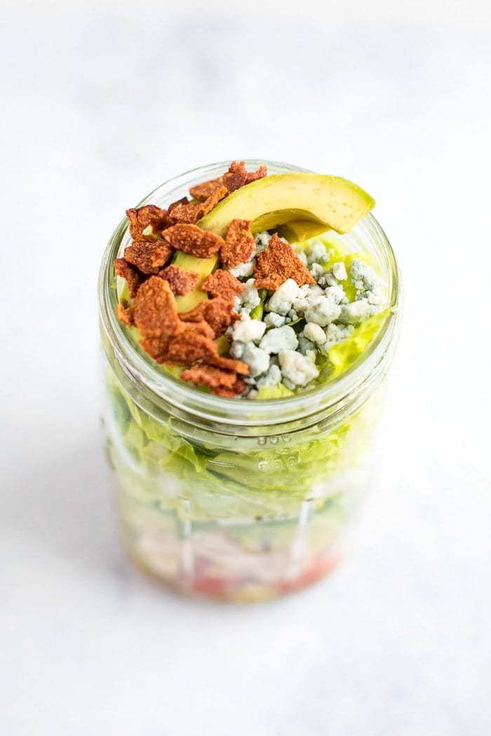 Overhead shot of the chicken avocado club mason jar salad. The turkey bacon, avocado and blue cheese are visible on top. 