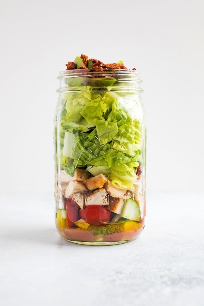 Mason jar salad with dressing, tomatoes, cucumbers, chicken, romaine, turkey bacon and avocado. 
