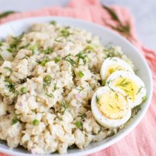 Cauliflower potato salad in a white bowl with three slices of hardboiled egg on the side.