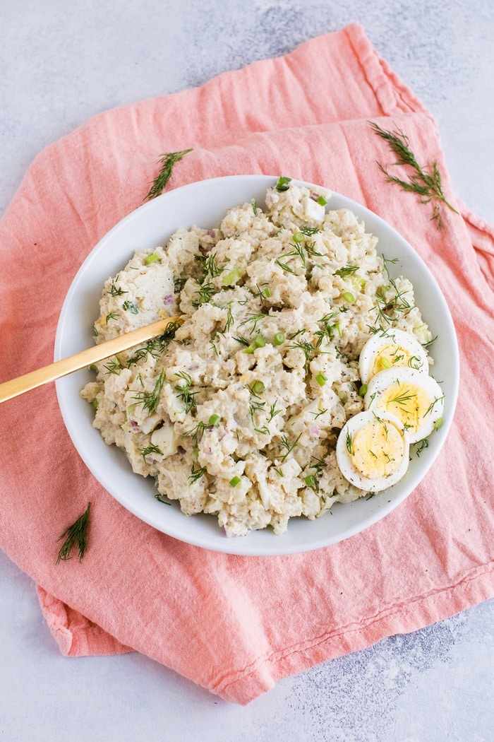 Cauliflower potato salad in a white bowl with three slices of hardboiled egg on the side. 