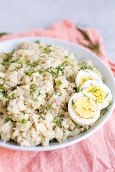 Cauliflower potato salad in a white bowl with three slices of hardboiled egg on the side.