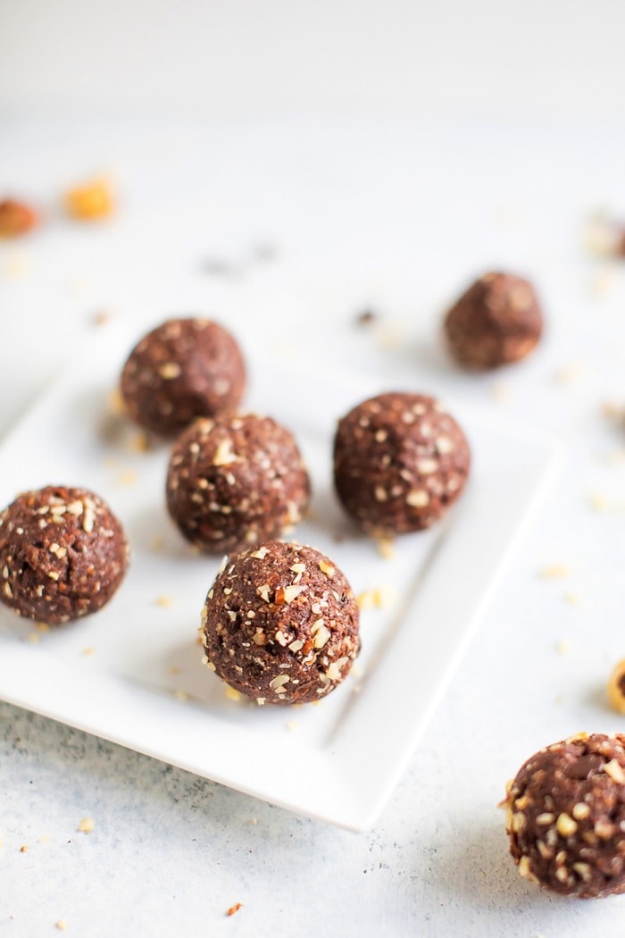 Homemade chocolate hazelnut energy bite in front with additional energy bites in the background on a white plate. 