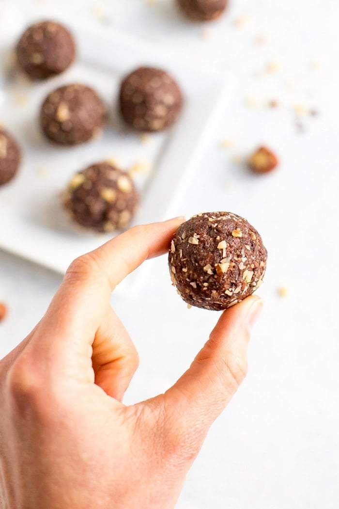 PIN THIS --> Healthy Homemade Ferrero Rocher Bites Homemade chocolate hazelnut energy bite being held by a woman's hand.