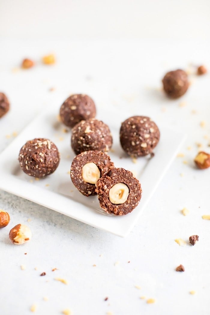 Homemade chocolate hazelnut energy bite in front, chopped in half to show the hazelnut in the center of the bite. 