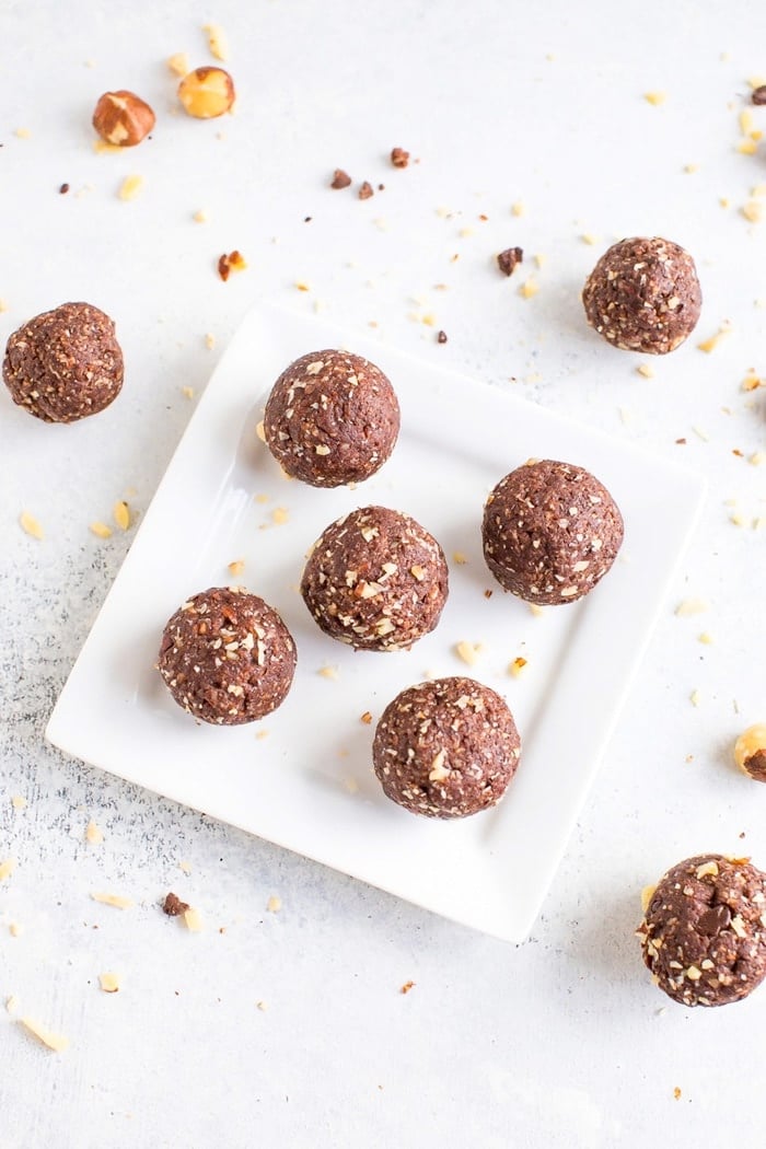 Overhead shot of homemade chocolate hazelnut energy bites on a white plate with hazelnuts around the plate.