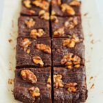 No bake brownies topped with walnuts and a chocolate drizzle on parchment.