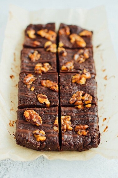 No bake brownies topped with walnuts and a chocolate drizzle on parchment.