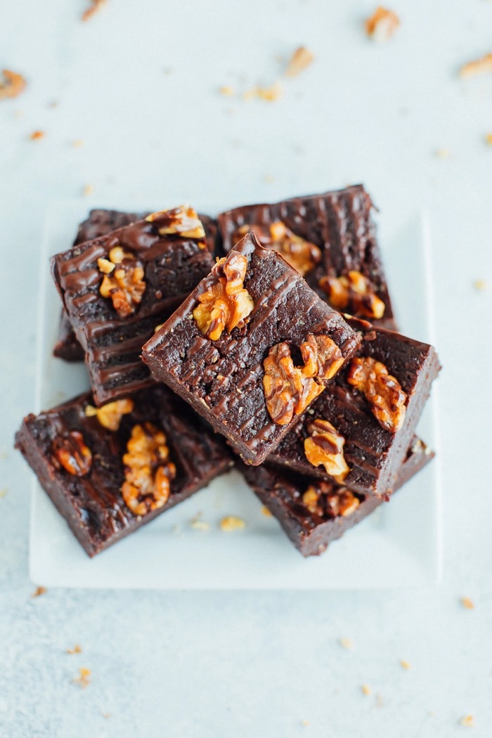 No bake brownies topped with walnuts and a chocolate drizzle on a small white square plate. 