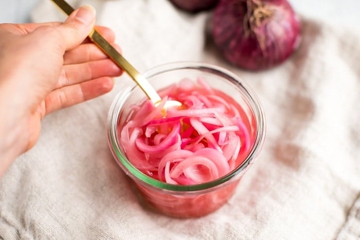 Pickled red onions in a weck jar with a gold fork and full red onions in the background.