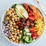 Vegan cobb salad with tempeh bacon and chickpeas in a white bowl with a gold fork.