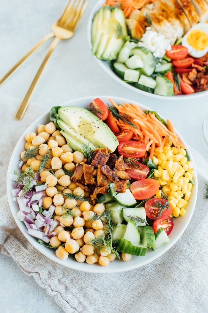 Vegan cobb salad in a white bowl with two gold forks in the background. 