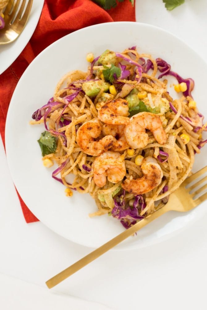 Chili lime shrimp and corn on top of a plate of spiralized jicama noodles. A gold folk in resting on the plate.