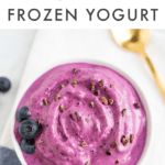 Bowl of blueberry and almond butter frozen yogurt toped with blueberries and cocao nibs. Gold spoon on the table. Text at the top reads "3-Ingredient Blueberry Frozen Yogurt"