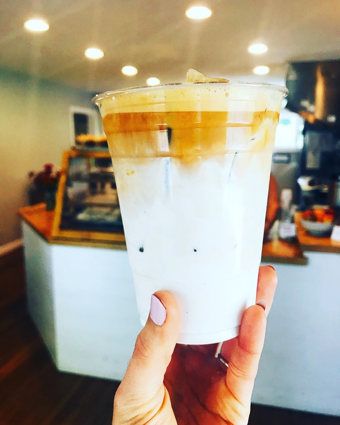 Hand holding a plastic cup filled with cream and nitro coffee.