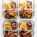 4 meal prep glass containers filled with orange slices, nutty trail mix, broccoli and peppers with ginger chicken.