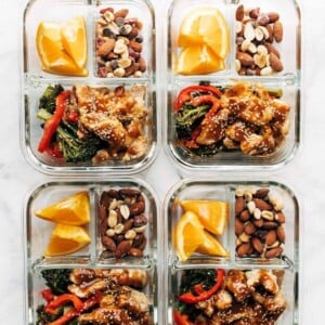 4 meal prep glass containers filled with orange slices, nutty trail mix, broccoli and peppers with ginger chicken.