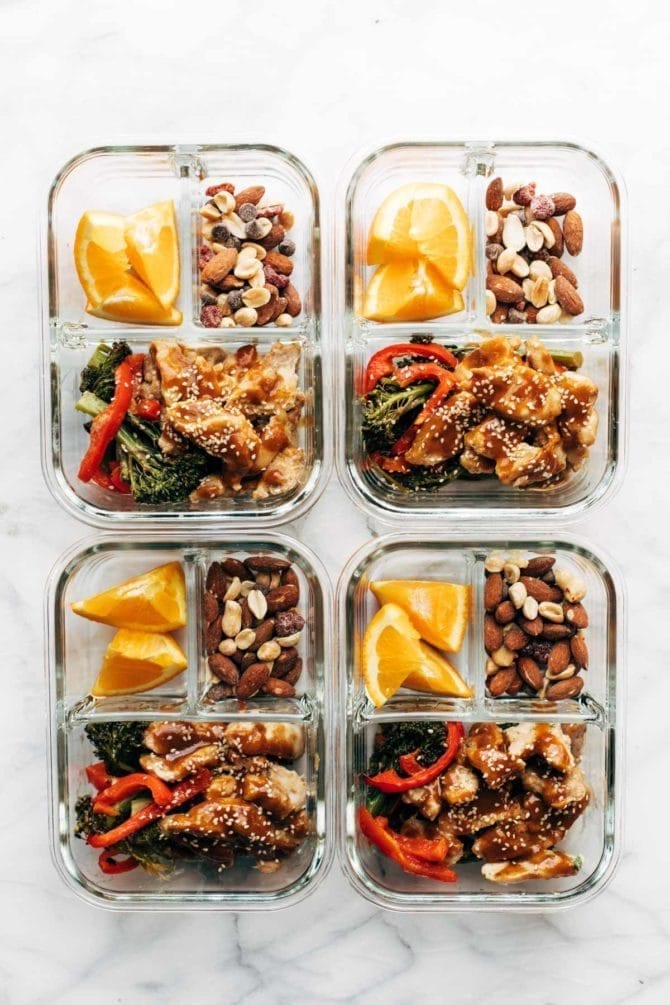 4 meal prep glass containers filled with orange slices, nutty trail mix, broccoli and peppers with ginger chicken.