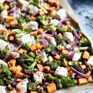 Sheet pan lined with parchment paper, with baked sweet potato cubes, broccoli, red onion and chicken cubes.