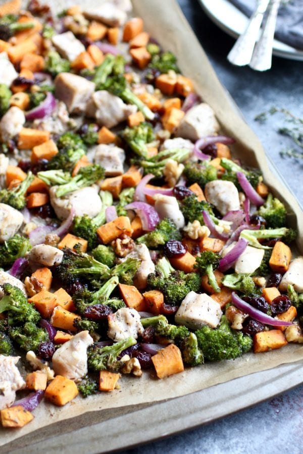 Sheet pan lined with parchment paper, with baked sweet potato cubes, broccoli, red onion and chicken cubes.