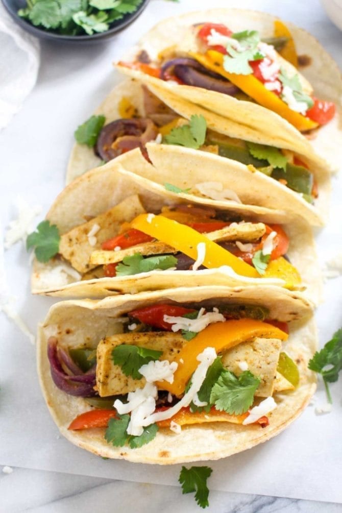 Three tacos filled with tofu, peppers, onions, cilantro, and cheese.