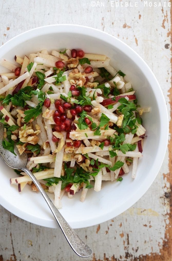 Jicama, apple and pomegranate salad topped with parsley in a large serving bowl with a silver serving spoon.