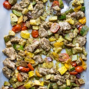 Sheet pan with parchment paper, with baked pesto chicken and tomatoes, zucchini and summer squash.