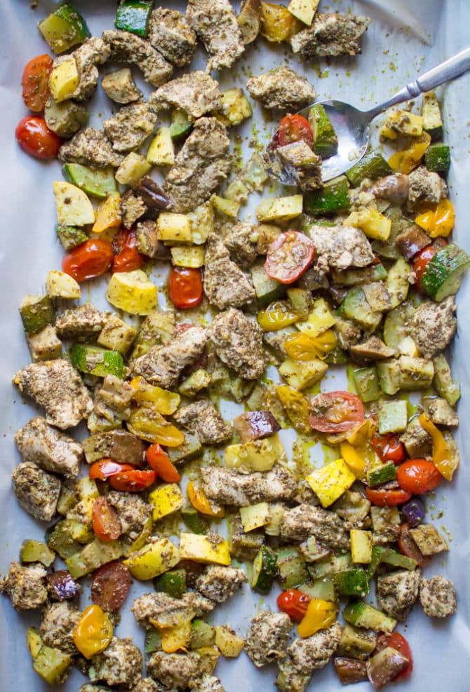 Sheet pan with parchment paper, with baked pesto chicken and tomatoes, zucchini and summer squash.