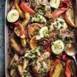 Sheet pan with baked chicken, peppers, potatoes, avocado slides and lime halves.