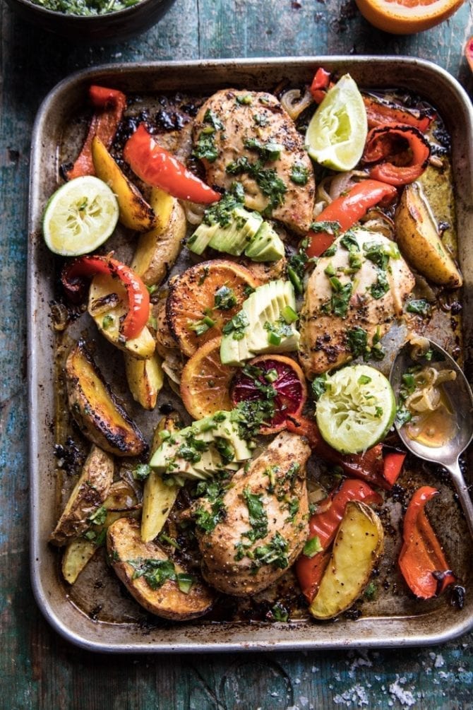 Sheet pan with baked chicken, peppers, potatoes, avocado slides and lime halves.