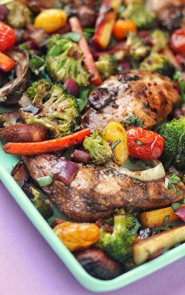 Sheet pan with baked balsamic chicken and broccoli, peppers, tomatoes, and herbs.