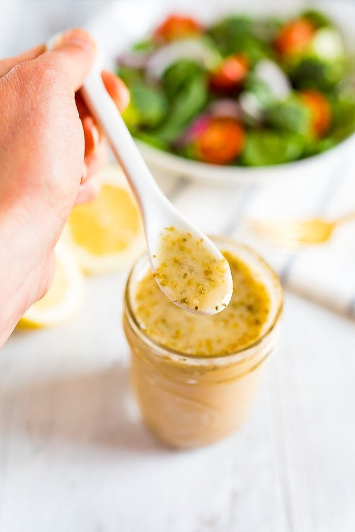 Lemon dressing in a small mason jar with a woman holding a white spoon. 