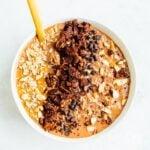 White bowl of chocolate peanut butter overnight oats with peanut butter, granola, peanuts and chocolate chips layered on top.