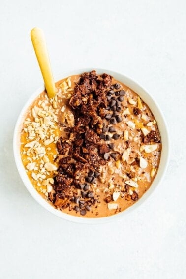 White bowl of chocolate peanut butter overnight oats with peanut butter, granola, peanuts and chocolate chips layered on top.