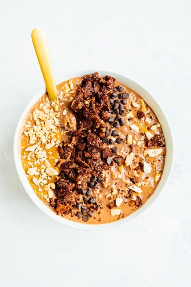 Bowl of chocolate peanut butter cup overnight oats with a spoon. Topped with peanuts, peanut butter, granola, and chocolate chips.