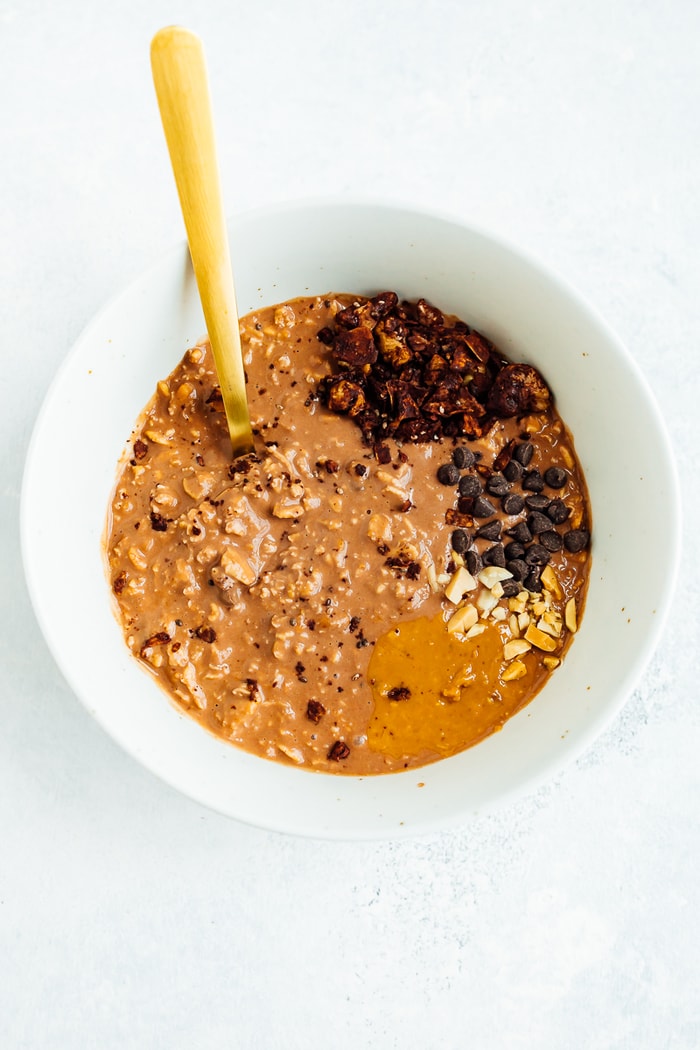 A white bowl filled with chocolate peanut butter overnight oats topped with peanut butter, chocolate chips and granola.