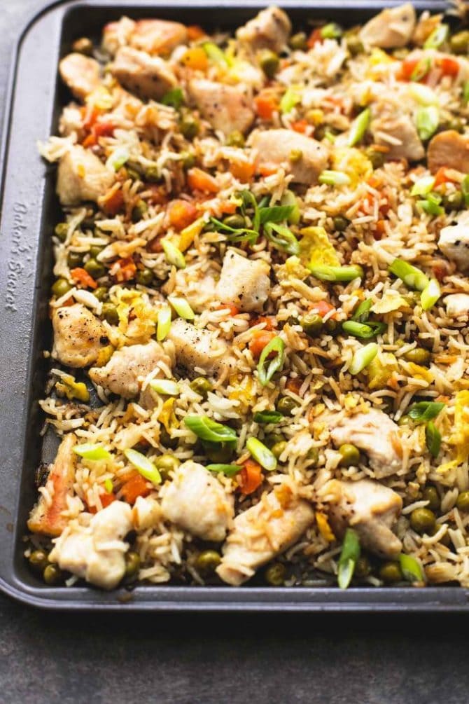 Sheet pan with baked chicken pieces, fried rice, scallions and mini pieces of carrots.