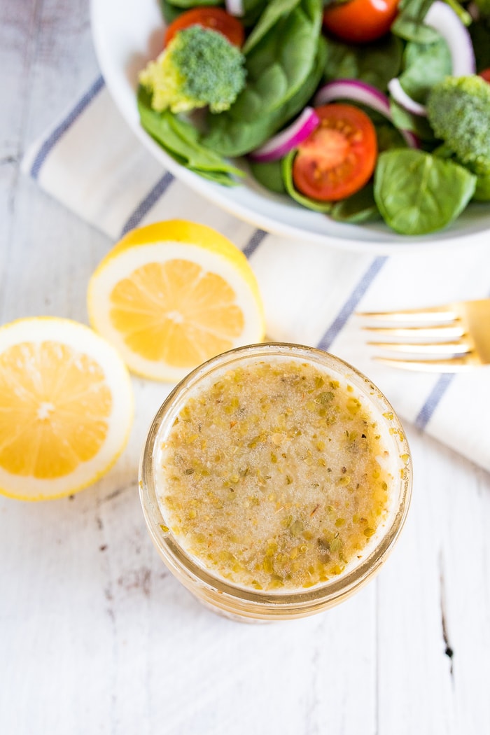 Overhead shot of lemon dressing in a small mason jar with salad and a gold fork in the background. 