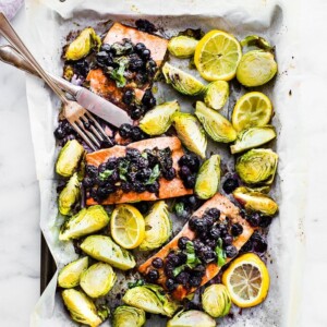 Sheet pan with parchment paper and silverware. Salmon baked with blueberries on top, Brussels sprouts and lemon.