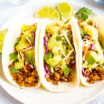 Three tempeh tacos with avocado and tomatillo dressing on a plate.