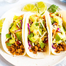 Three tempeh tacos with avocado and tomatillo dressing on a plate.