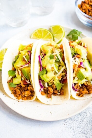 Three tempeh tacos with avocado and tomatillo dressing on a plate.