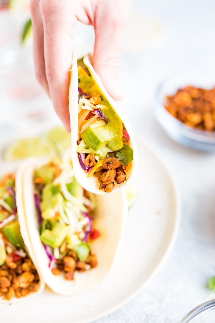 Hand holding one tempeh taco topped with avocado, cilantro, and tomatillo dressing.